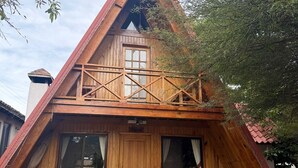 A wooden house with a sloped roof, a balcony, and a small garden area. - CABAÑAS BERNAL & HOTEL & SUITES (Quéretaro)