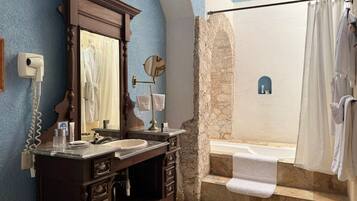 A bathroom with a stone wall, a bathtub, a shower, a vanity with a mirror, and a towel rack.