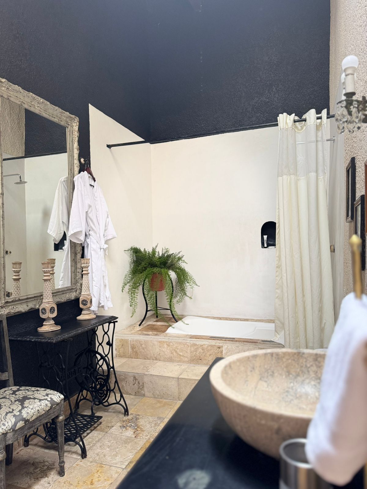 Un baño con un espejo grande, un tocador negro, una bañera blanca y una planta en maceta.