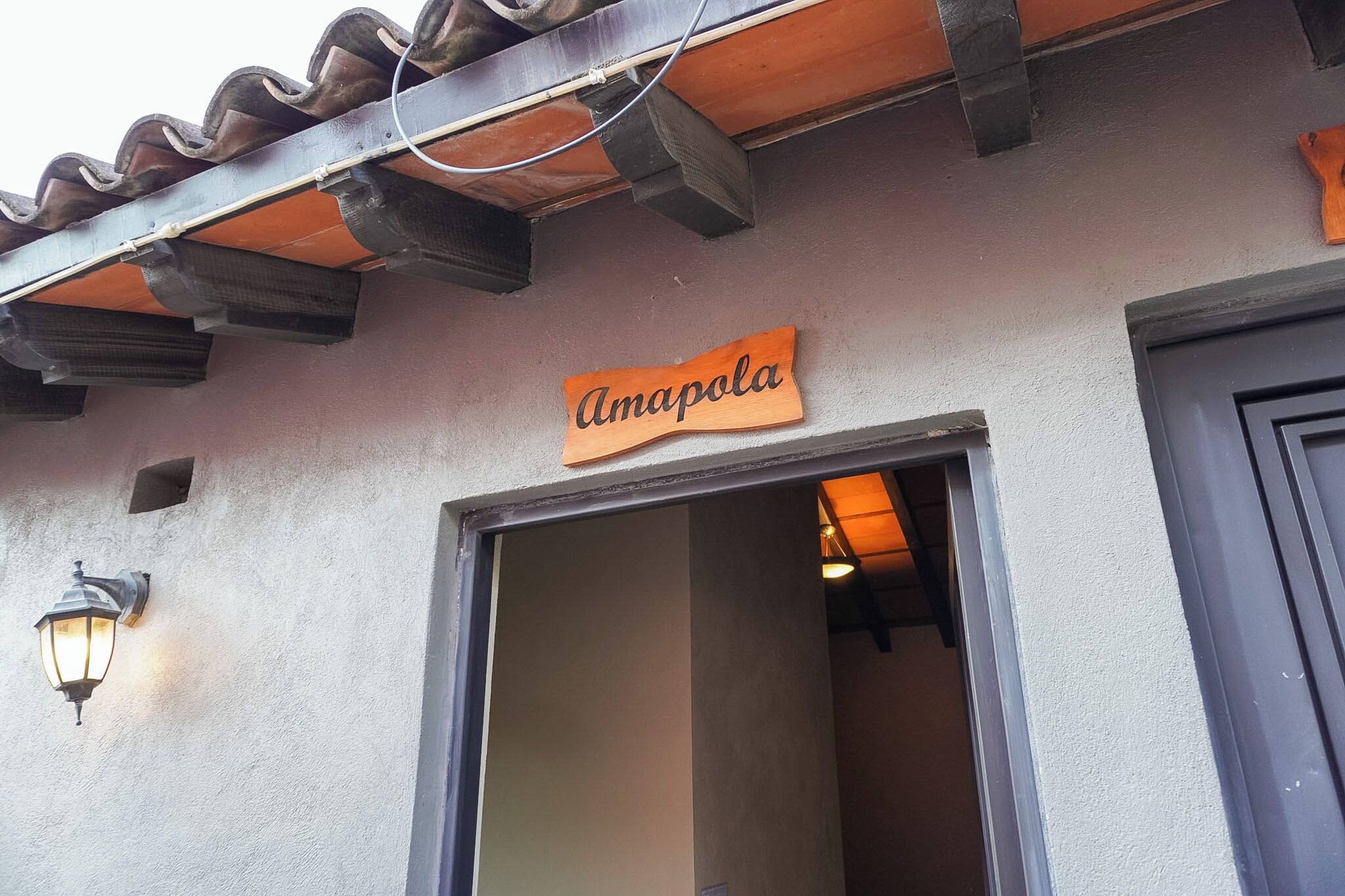 Una entrada de edificio con un letrero que dice 'Amapola' y una lámpara de pared.