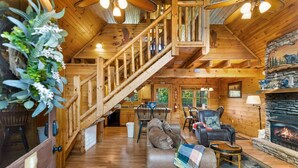A wooden cabin interior with a staircase, living room, fireplace, and dining area. - Southern Style - Hot Tub with TV, Game Room, Kids' Playhouse + Cornhole (Sevierville)