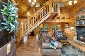 A wooden cabin interior with a staircase, living room, fireplace, and dining area. - Southern Style - Hot Tub with TV, Game Room, Kids' Playhouse + Cornhole (Sevierville)