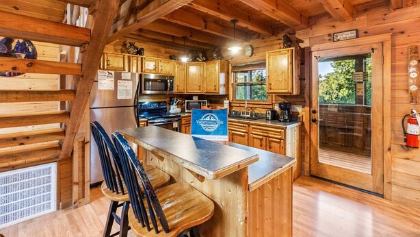 A wooden cabin interior with a kitchen area, bar seating, and a sign indicating vacation rentals. - Southern Style - Hot Tub with TV, Game Room, Kids' Playhouse + Cornhole (Sevierville)