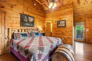 A wooden cabin bedroom with a bed, a painting, a framed picture, and a barrel. - Southern Style - Hot Tub with TV, Game Room, Kids' Playhouse + Cornhole (Sevierville)