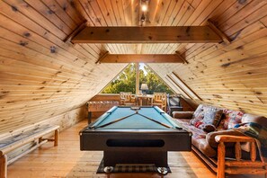 An attic room with a pool table, a sofa, and a view of the outdoors. - Southern Style - Hot Tub with TV, Game Room, Kids' Playhouse + Cornhole (Sevierville)
