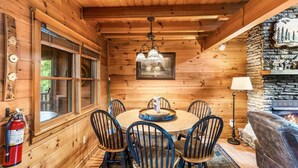 A wooden cabin interior with a dining table, chairs, a chandelier, a fireplace, and a fire extinguisher. - Southern Style - Hot Tub with TV, Game Room, Kids' Playhouse + Cornhole (Sevierville)