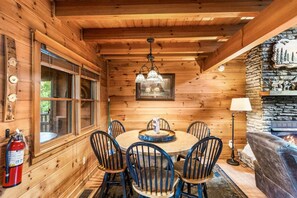 A wooden cabin interior with a dining table, chairs, a chandelier, a fireplace, and a fire extinguisher. - Southern Style - Hot Tub with TV, Game Room, Kids' Playhouse + Cornhole (Sevierville)