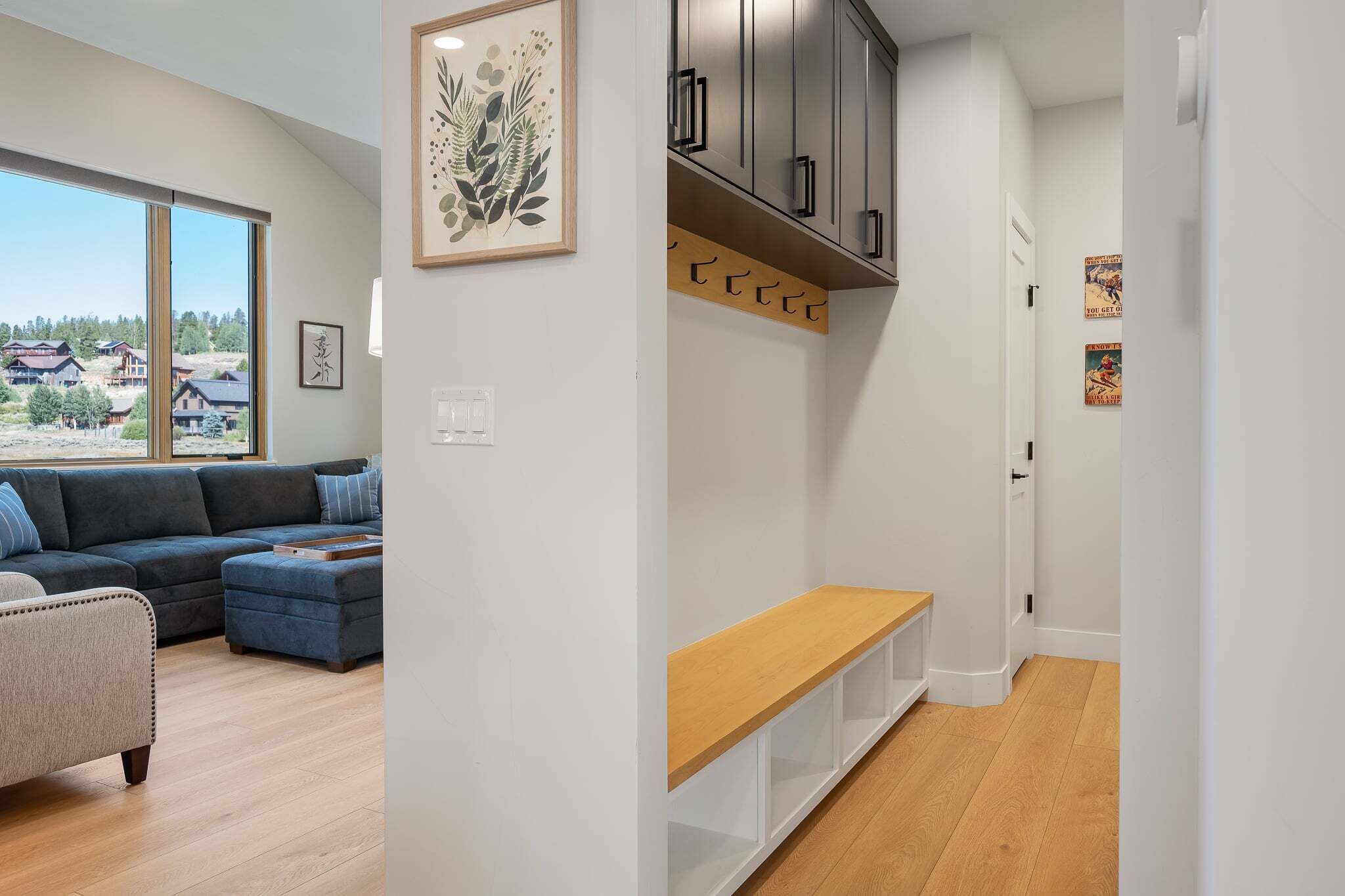 Un salon moderne avec un canapé d’angle, un banc en bois et une vue sur les maisons à travers de grandes fenêtres.