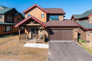A two-story wooden house with a front porch, a garage, and a driveway. - Coyote Creek 1602 I Private Hot Tub I Great Views I Bunk Room I Discounted Attractions (Tabernash)