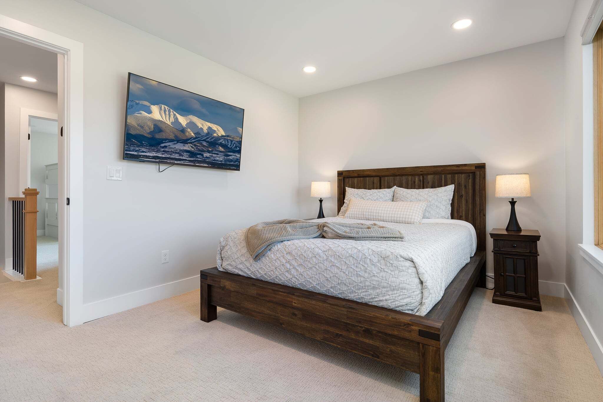 A bedroom with a bed, two bedside lamps, a painting on the wall, and a door leading to another room.