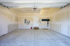 Eine Garage mit weißer Tür, einer Deckenkamera und einem schwarzen Metallregal mit Werkzeugen.