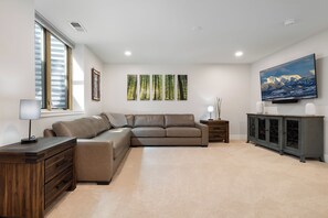 A modern living room with a sectional sofa, a flat-screen TV, and a large window. - Coyote Creek 1602 I Private Hot Tub I Great Views I Bunk Room I Discounted Attractions (Tabernash)