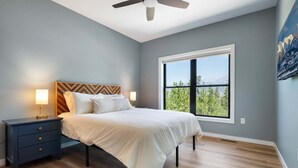 A bedroom with a bed, nightstands, a ceiling fan, and a large window with a view. - Milky Way Mountain Chalet I Private Hot Tub I Great Views I Bunk Room I Discounted Attractions (Fraser)