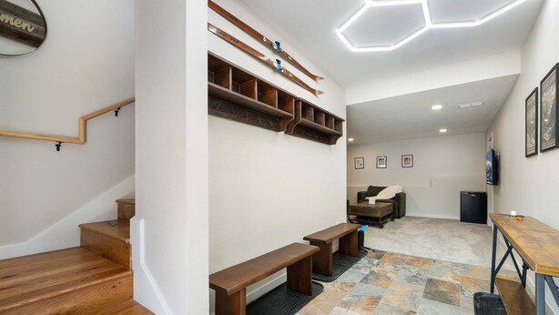 A modern interior with a staircase, wooden benches, a seating area, and a wall-mounted ski rack. - Milky Way Mountain Chalet I Private Hot Tub I Great Views I Bunk Room I Discounted Attractions (Fraser)