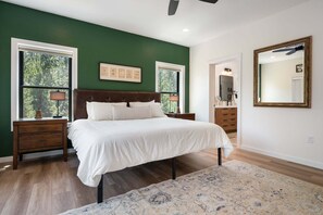 Una camera da letto con un letto grande, due comodini, una cassettiera, uno specchio e una finestra con vista sugli alberi.