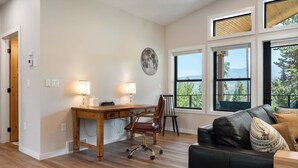 A room with a wooden desk, two lamps, a leather chair, a black leather sofa, and large windows with a view of trees and mountains. - Milky Way Mountain Chalet I Private Hot Tub I Great Views I Bunk Room I Discounted Attractions (Fraser)