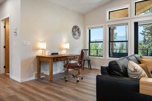 A room with a wooden desk, two lamps, a leather chair, a black leather sofa, and large windows with a view of trees and mountains. - Milky Way Mountain Chalet I Private Hot Tub I Great Views I Bunk Room I Discounted Attractions (Fraser)