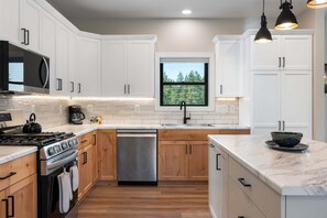 Una cucina moderna con mobili bianchi, una lavastoviglie in acciaio inossidabile, un fornello e una finestra vista alberi.