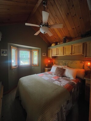 A bedroom with a bed, wooden ceiling, and a window with blinds.