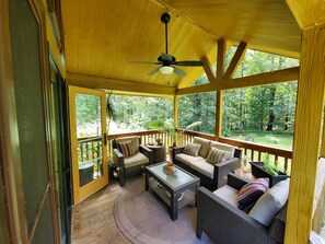 A covered porch with wicker furniture, a ceiling fan, and a view of a forested area. - Bison Farm - Cabin "Vieja" (Culpeper)