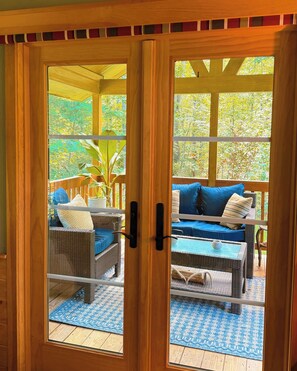 A wooden-framed glass door leading to an outdoor patio with wicker furniture and a blue rug. - Bison Farm - Cabin "Vieja" (Culpeper)