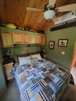 A cabin-style bedroom with a wooden ceiling, a bed with a quilt, wooden cabinets, and a ceiling fan. - Bison Farm - Cabin "Vieja" (Culpeper)