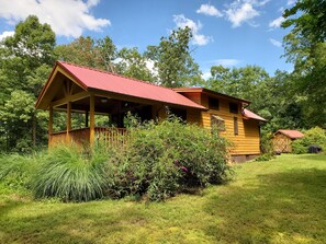 A wooden cabin with a red roof, surrounded by lush greenery and trees. - Bison Farm - Cabin "Vieja" (Culpeper)