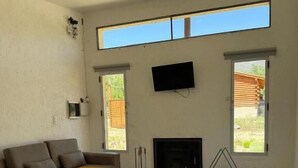 A living room with a sofa, a glass table, yellow chairs, a fireplace, and a TV mounted on the wall.