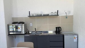 A compact kitchenette with a microwave, toaster, and refrigerator. There is a small dining table with chairs.