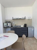 Cozinha compacta equipada com micro-ondas, torradeira e frigorífico. Inclui uma pequena mesa de jantar com cadeiras.