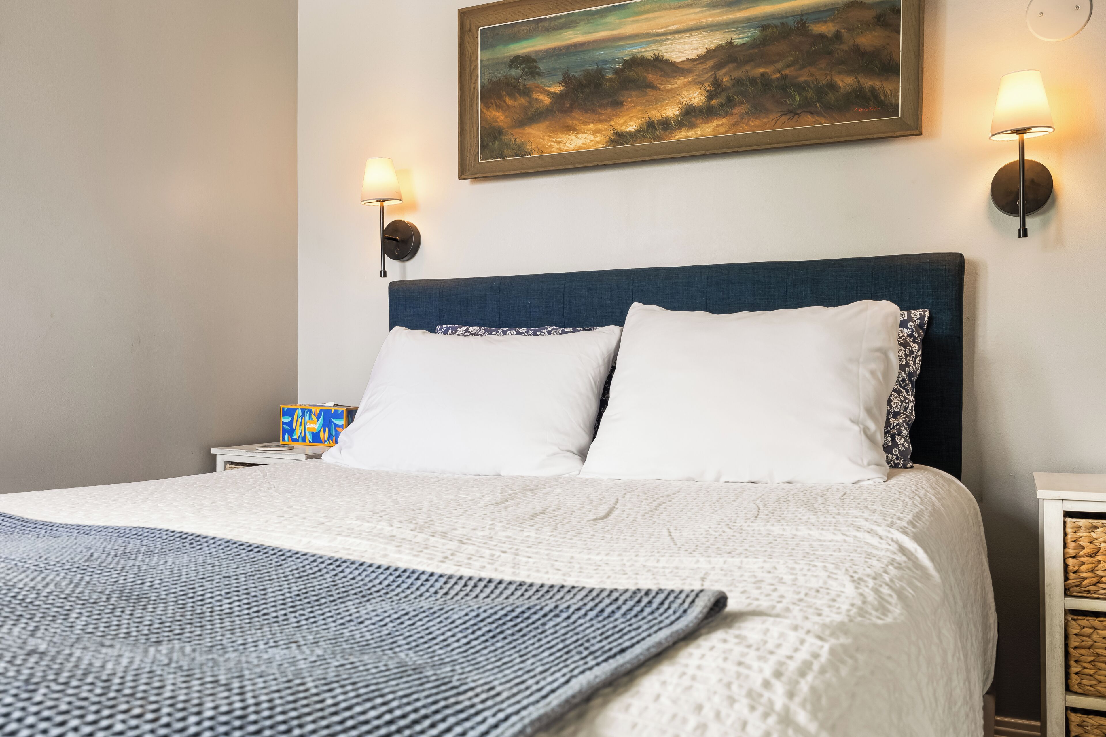 Un lit avec une literie blanche, une tête de lit bleue et deux lampes fixées au mur.