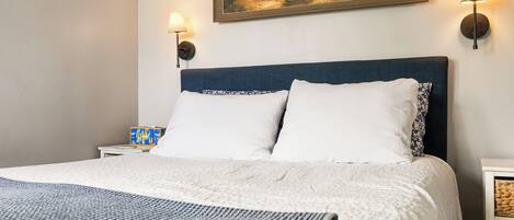 Un lit avec une literie blanche, une tête de lit bleue et deux lampes fixées au mur.