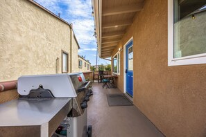 A narrow outdoor corridor with a barbecue grill, a table with chairs, and a blue door. - 1 Block to Beach | Charming 2BR Newport Bungalow w/ Patios, Bikes & Gear (Newport Beach)