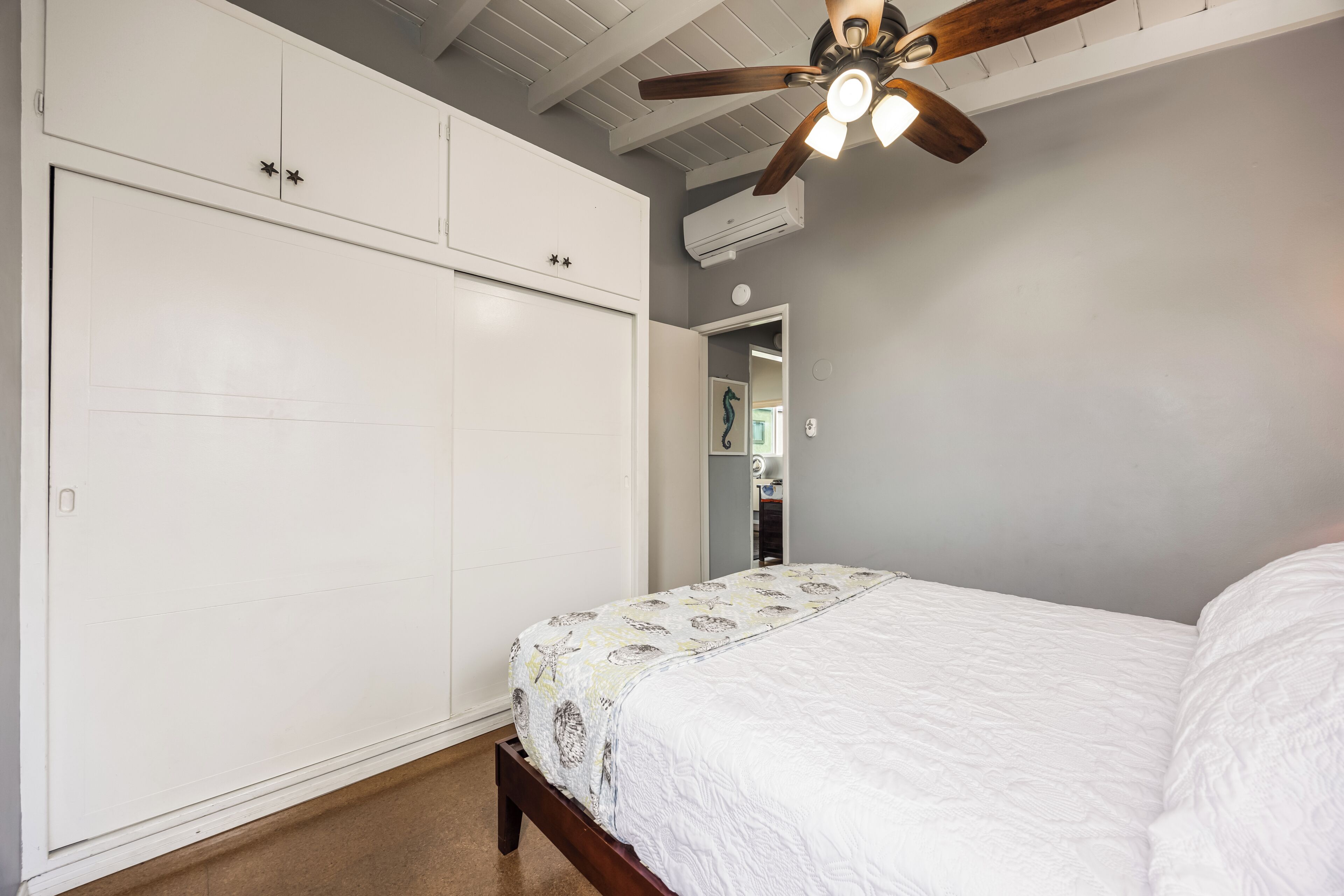 Un dormitorio con cama, armario, ventilador de techo y puerta que da a otra habitación.