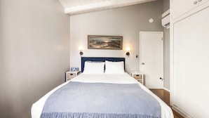 Un dormitorio con cama, dos mesitas de noche, un cuadro en la pared y una puerta.