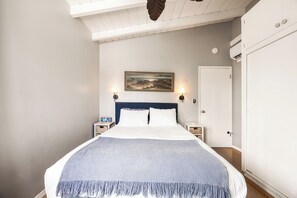 A bedroom with a bed, two bedside tables, a painting on the wall, and a door. - 1 Block to Beach | Charming 2BR Newport Bungalow w/ Patios, Bikes & Gear (Newport Beach)