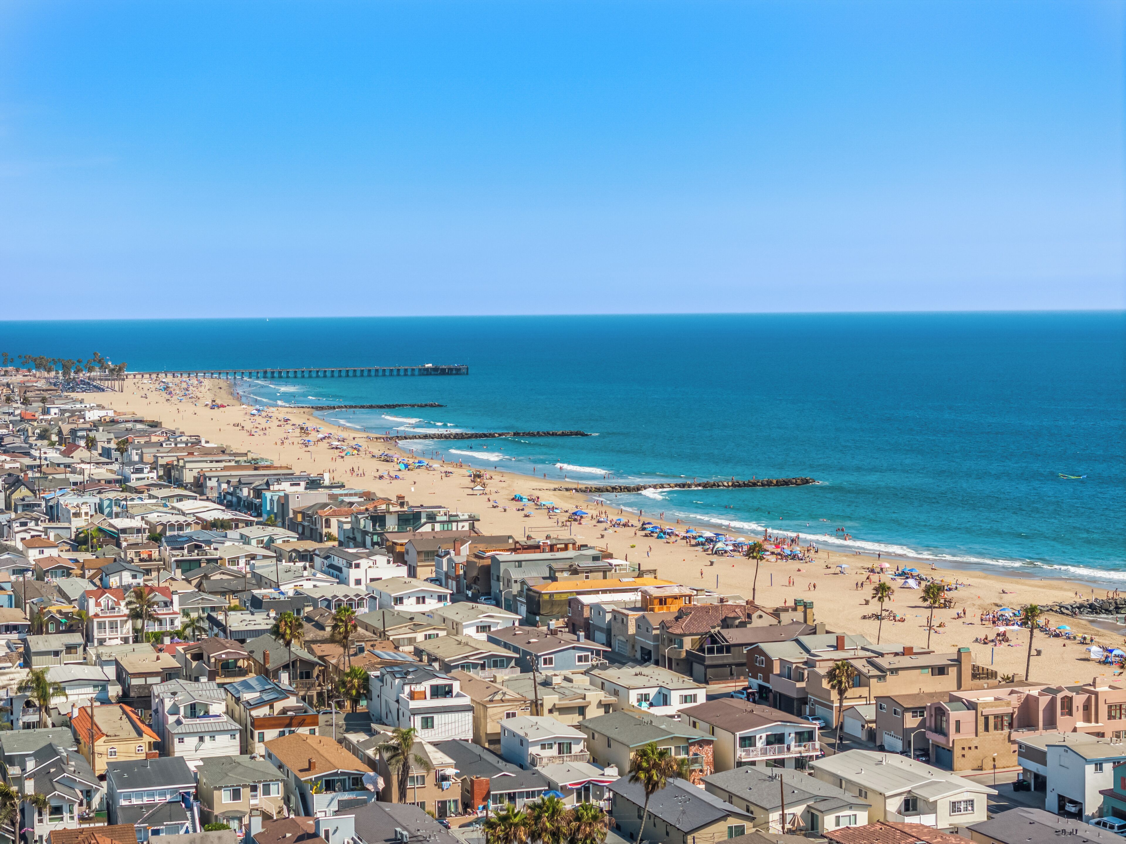 A coastal residential area with houses, a beach, and a pier.