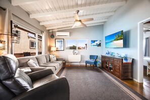 A living room with a leather sofa, a coffee table, a TV, and a ceiling fan. - 1 Block to Beach | Charming 2BR Newport Bungalow w/ Patios, Bikes & Gear (Newport Beach)