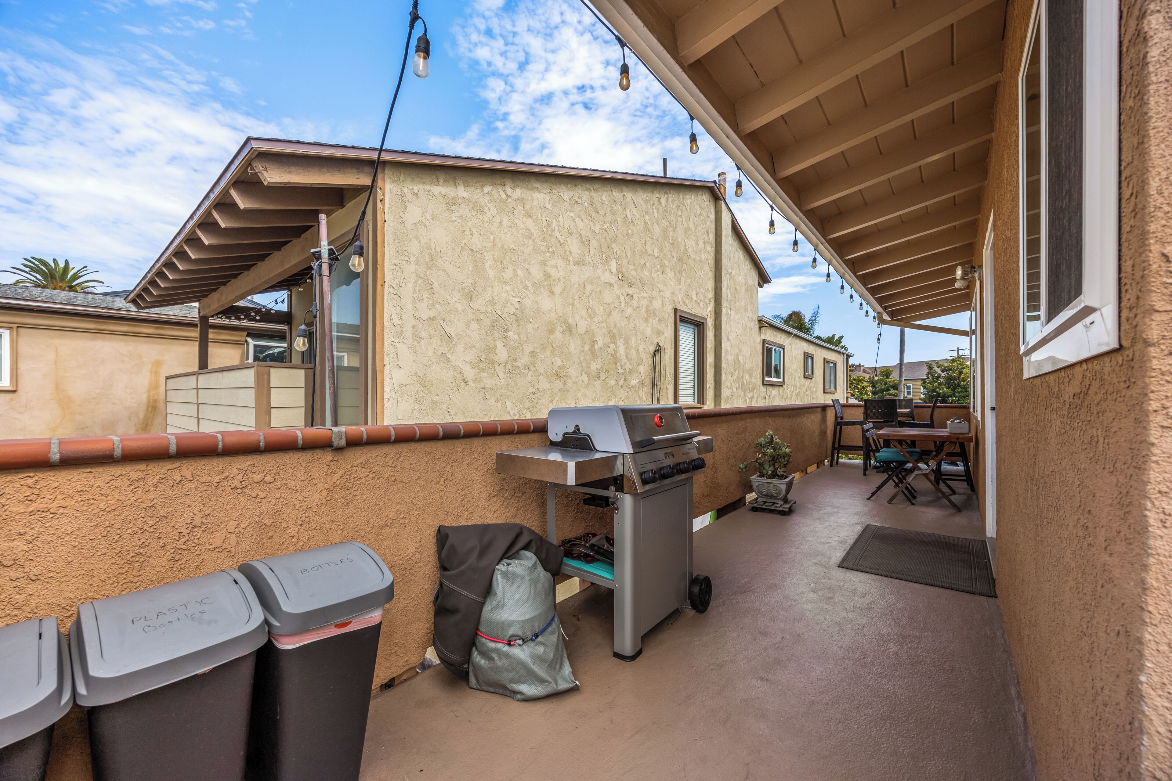 Un espace extérieur aménagé en terrasse, avec un barbecue, des poubelles et une table avec des chaises.