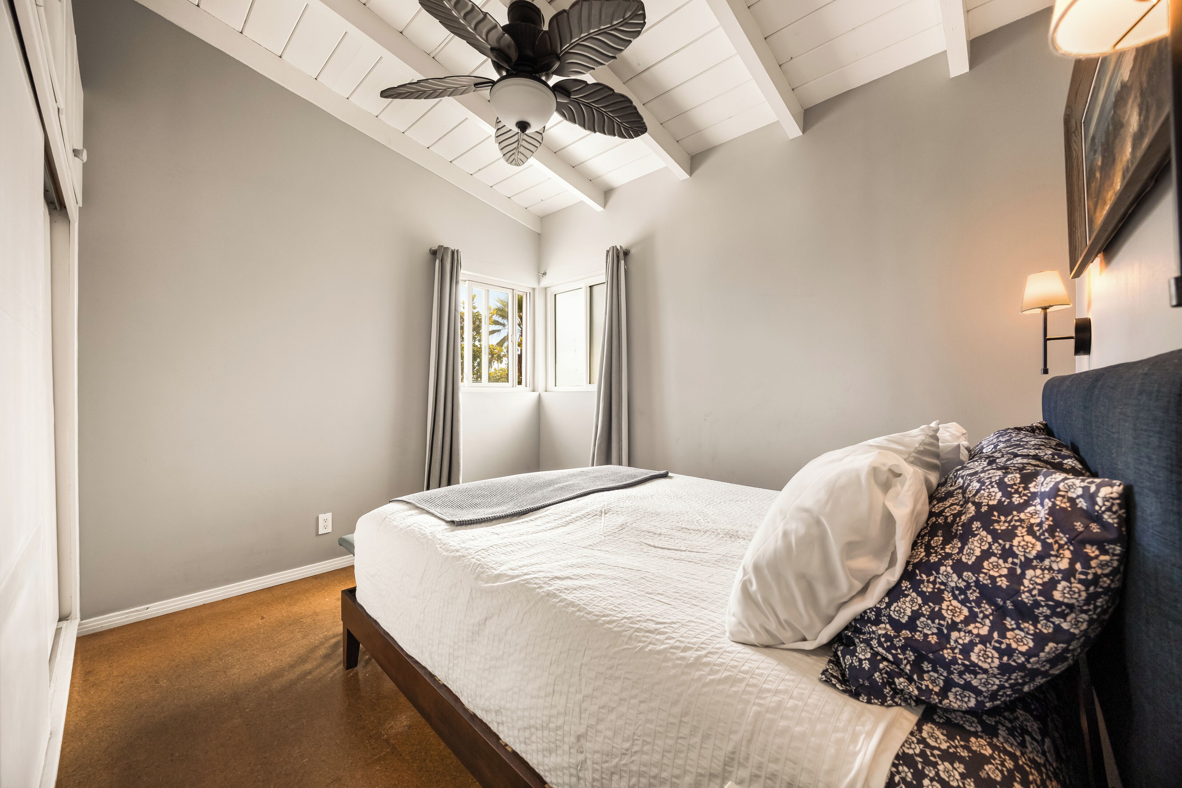 Um quarto com cama, cortinas, ventoinha no teto e mesa de cabeceira com abajur.
