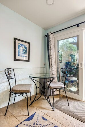 A small room with a glass table and two chairs, a framed picture on the wall, and a sliding glass door leading to an outdoor area. - 1 Block to Beach | Newport Beach Studio w/ Modern Bath, Courtyard & Bikes (Newport Beach)
