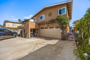 A two-story house with a garage, a driveway, and a front yard with a tree and a blue gate. - 1 Block to Beach | Newport Beach Studio w/ Modern Bath, Courtyard & Bikes (Newport Beach)