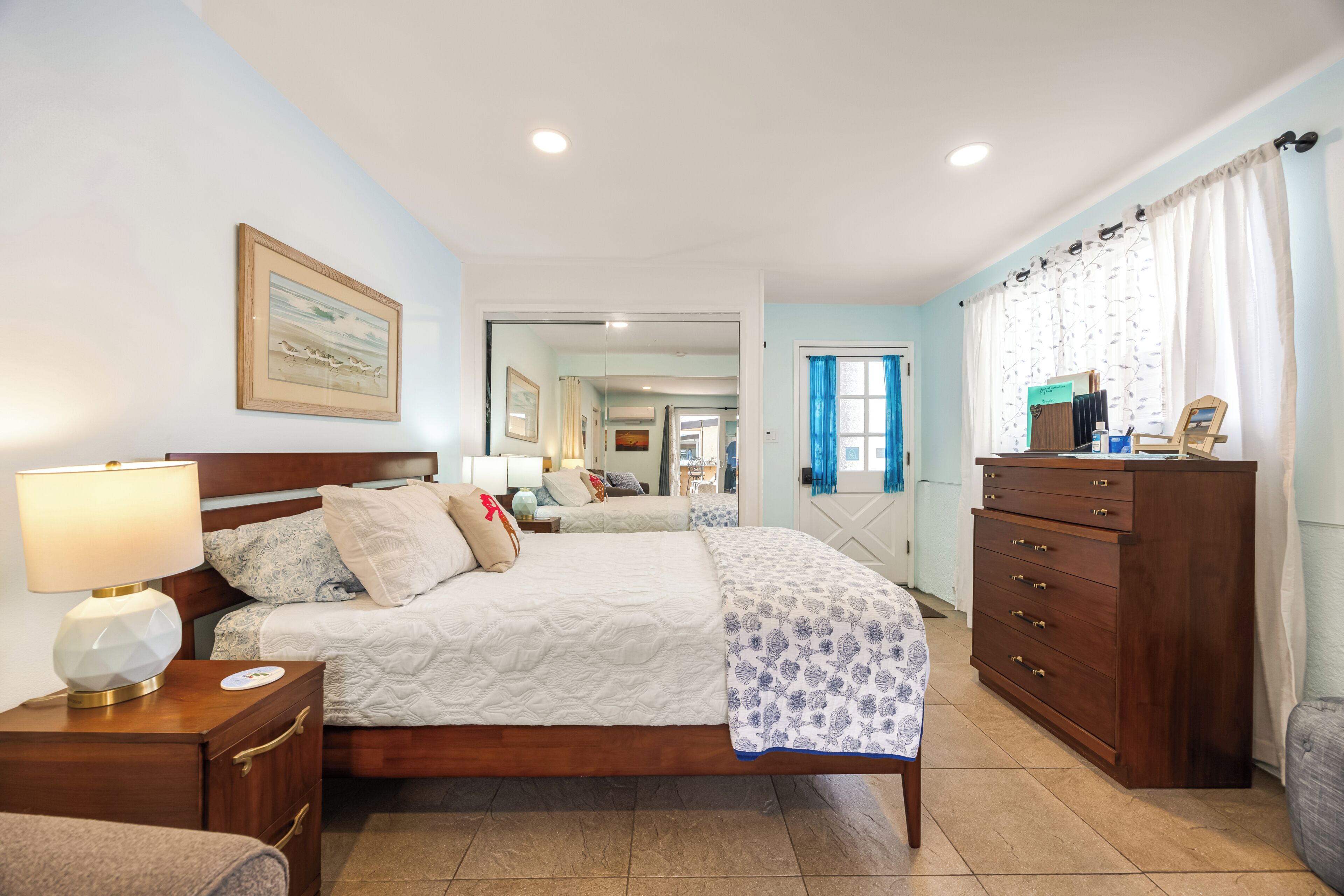A hotel room with a bed, bedside table, lamp, dresser, and a mirror.