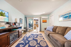 A living room with a sofa, a coffee table, a TV, and a dining area visible through a glass door. - 1 Block to Beach | Newport Beach Studio w/ Modern Bath, Courtyard & Bikes (Newport Beach)