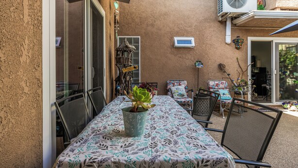 Eine Terrassengruppe im Freien mit Tisch für zwei Personen, umgeben von Stühlen, einem dekorativen Vogelhäuschen und einem kleinen Garten.