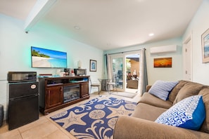 Sala de estar con sofá, televisor, zona de cocina y vistas a través de un ventanal.