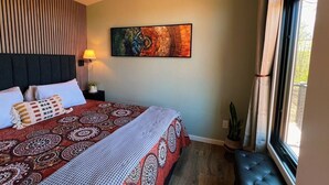 Een hotelkamer met een bed, een schilderij aan de muur, een bedlampje en een raam met gordijnen.