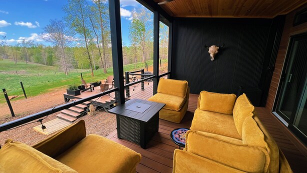 Een overdekt terras met gele fauteuils en een tafel, met uitzicht op een grasrijk landschap.