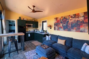 A modern living room with a dark blue sofa, a wooden coffee table, and a large abstract painting on the wall. - Bison Farm - Vista Cabin (1 BR option) (Culpeper)