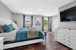 A bedroom with a bed, a dresser, a television, and a window with curtains. - the bourbon barrel escape HotTub Game Room pets ok (Shelbyville)